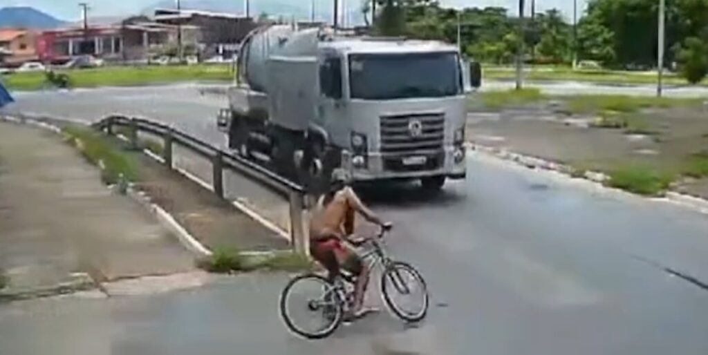 Ciclista colide em caminhão ao entrar em rotatória, cai na pista, levanta e sai pedalando